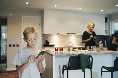 Boy using mobile phone while standing against parents in background