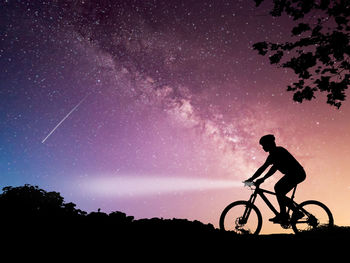 Silhouette man with bicycle against sky at night