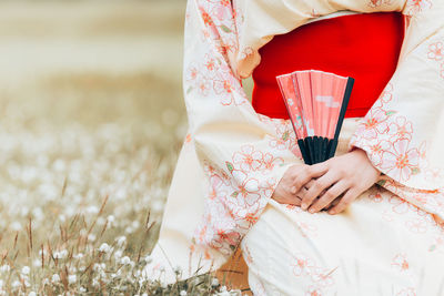 Midsection of woman holding hand fan while sitting on field