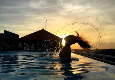 Woman in swimming pool against sky during sunset