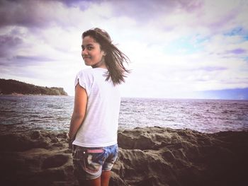 Young woman standing at beach against sky