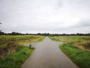 Empty road amidst field against sky