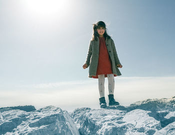 Full length of girl standing on rocks against sky during winter