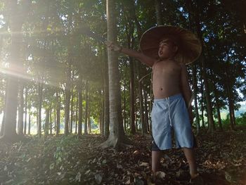 Full length of shirtless boy holding weapon standing in forest