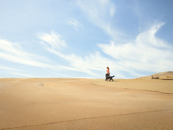 Woman walking dog at sand dune