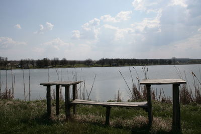 Empty bench at lakeshore against sky