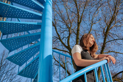 Woman standing by tree against blue sky