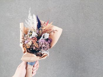 Cropped hand holding bouquet against wall