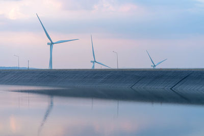 Wind turbines by lake against sky