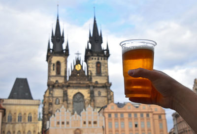 Cropped hand of man holding beer glass against cathedral