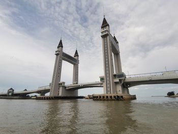 Low angle view of bridge over river against cloudy sky