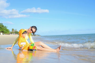 Side view of woman sitting on beach against sky