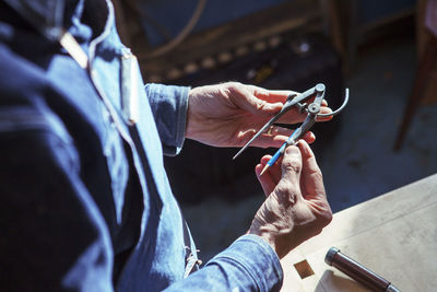 Midsection of carpenter holding compass at workshop