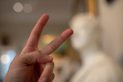 Cropped hand of person hand gesturing against statue