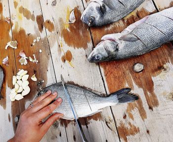 Cropped hand of woman chopping fish on wooden table