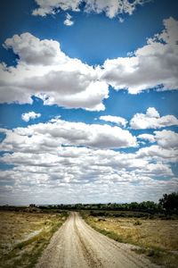 Road passing through field against cloudy sky