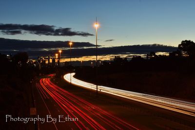 Light trails on road in city against sky at night