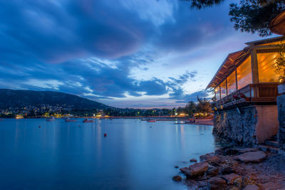 Illuminated city by sea against sky at sunset