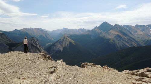 Rear view of hiker standing on peak by mountains against sky