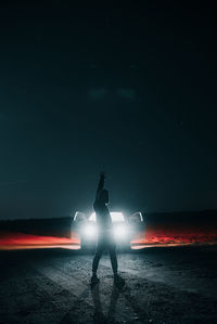 Silhouette man standing on illuminated street light against sky at night