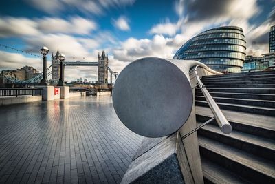 Footpath leading towards tower bridge against cloudy sky