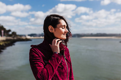 Young woman looking away while standing by lake against sky