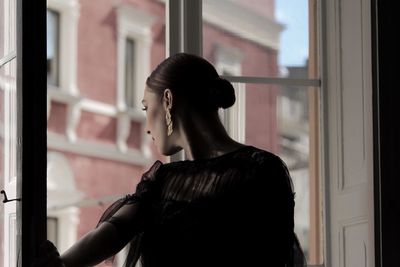 Rear view of woman standing by window at home