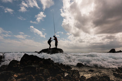 Men standing on rock by sea against sky