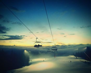 Ski lift over snow covered field against sky during sunset