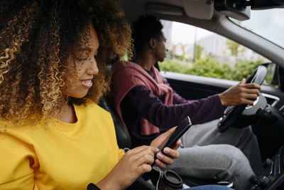 Woman using smart phone and friend driving car on road trip