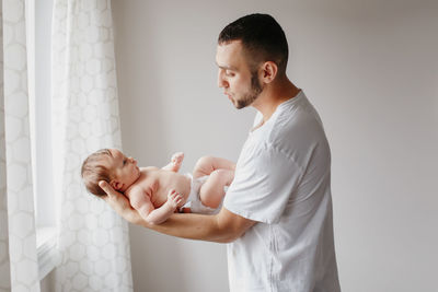 Father holding daughter in hands against wall at home