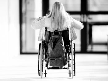 Rear view of woman with backpack sitting on wheelchair