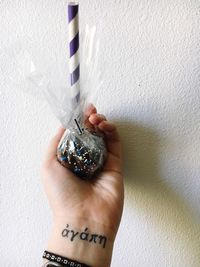 Cropped hand of woman holding object covered with plastic against wall