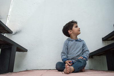 Boy looking away while sitting on wall