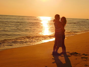 Couple embracing while standing at beach during sunset