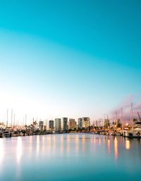 View of cityscape by sea against clear blue sky