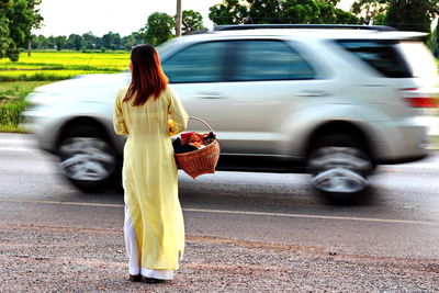 Rear view of vietnamese woman standing by car on road