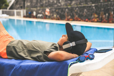 Boy listening music while resting on poolside