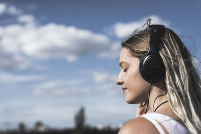 Young woman listening to music against sky