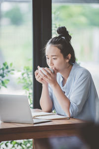 Businesswoman drinking coffee while looking at laptop in cafe