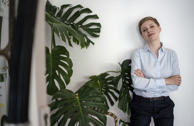 Portrait of a confident businesswoman standing at a wall beside a plant