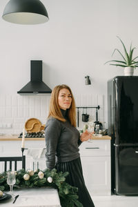 Mid-aged woman with glass on the kitchen decorated for christmas. beautiful female enjoying morning