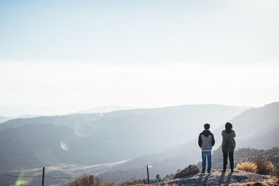 Rear view of man and woman standing on mountain against sky