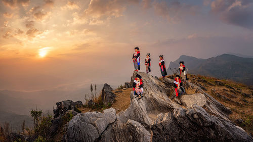 People on rock against sky during sunset