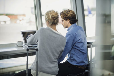 Rear view of business colleagues using laptop at airport cafe