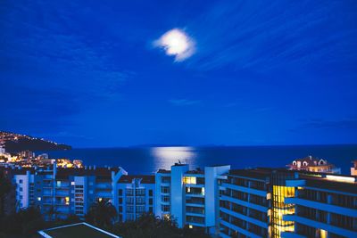 Illuminated city by sea against sky at night