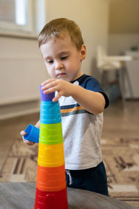 A cute little boy is playing with a multi-colored pyramid indoors. 