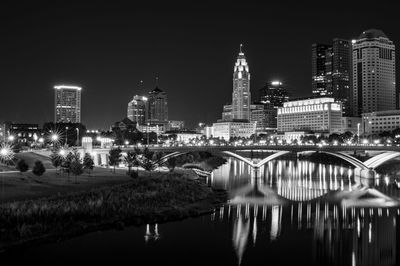 Illuminated buildings by river against sky in city at night