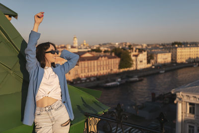 Rear view of young woman with arms raised standing by railing