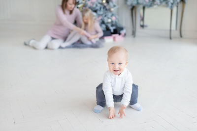 Portrait of cute baby boy crouching on tiled floor at home
